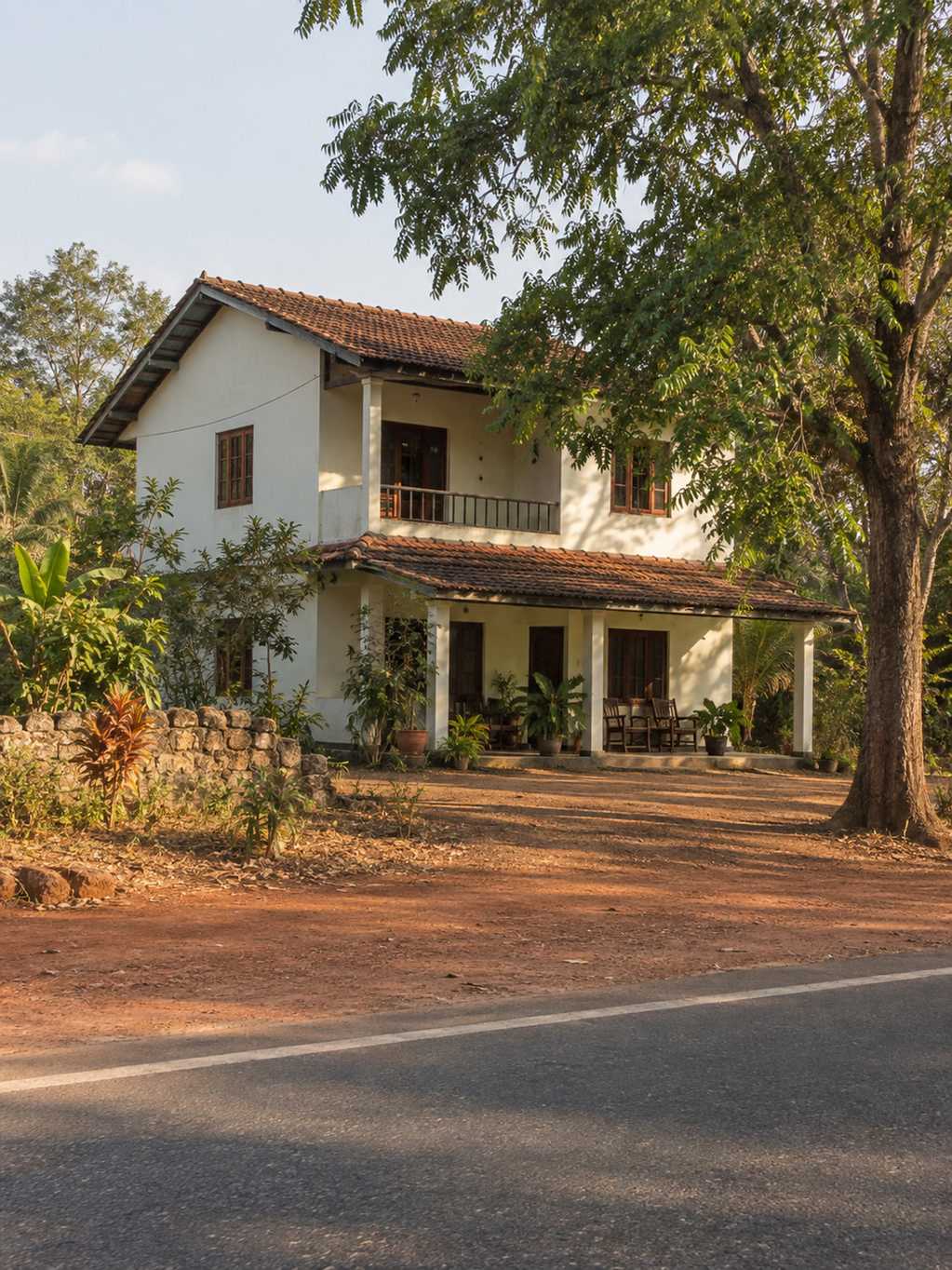 Two-storey roadside guesthouse on the A9 at Dambulla, laterite verge and a neem tree, late afternoon